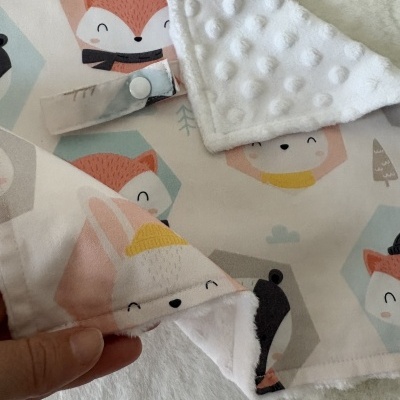 Manta de bebé com padrão de animais coloridos e interior branco com textura bolinhas.
