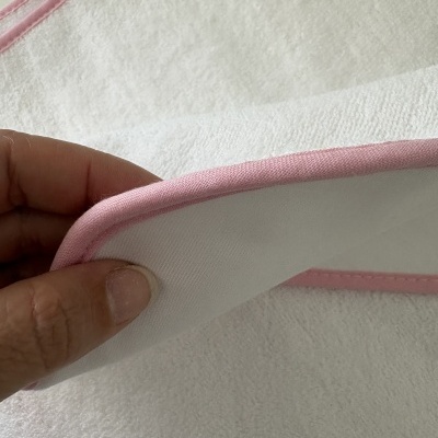 Toalha branca com borde rosa e textura felpuda, segurada por uma mão