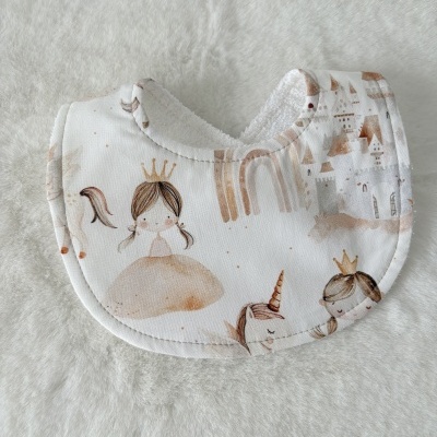Babete para bebé branco com estampados de bonecas, unicórnio e castelo em tons castanhos e bege