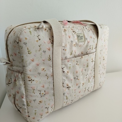 Mala floral bege com alças largas e etiqueta Mamá pintinho sobre superfície branca