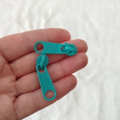 Dois puxadores de zíper azuis-turquesa na mão