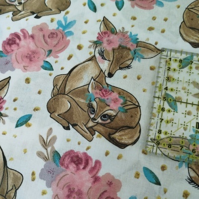 Tecido branco com estampa de veados e flores em tons castanhos, rosa e azul com pontos dourados e régua ao lado.