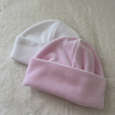 Dois gorros de bebé, um rosa e um branco, sobre superfície branca felpuda.
