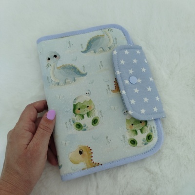 Capa azul claro com dinossauros estampados e fecho de botão azul com estrelas brancas