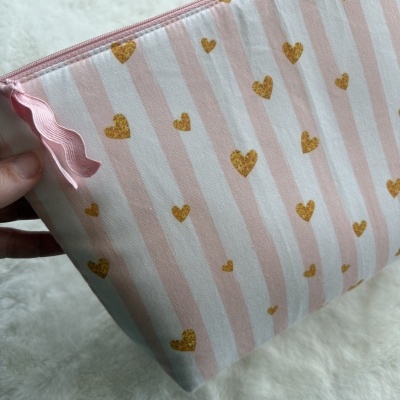 Estojo ou bolsa de tecido rosa com corações amarelos e riscas brancas.