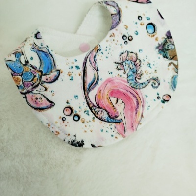 Babete de tecido com padrão colorido de sereias e animais marinhos