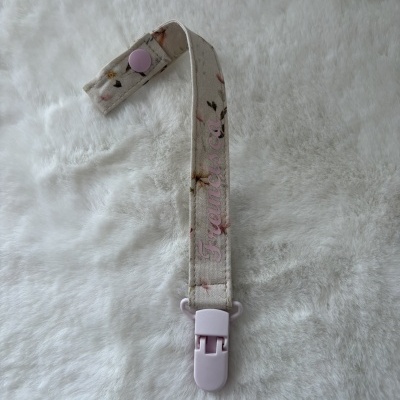 Tira de tecido floral bege com fecho de plástico rosa claro e botão de pressão.