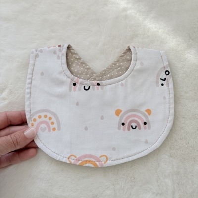 Babete branco com padrão de arcos coloridos e carinhas sorridentes, interior castanho com bolinhas brancas.