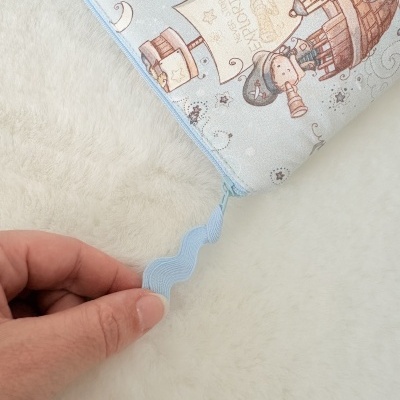 Estojo ou bolsa com padrão infantil azul e zip azul sendo segurado por uma mão