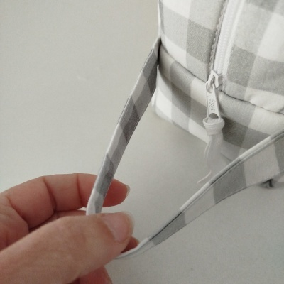 Bolsa de tecido xadrez cinza e branco com fecho de correr e alça segurada por mão