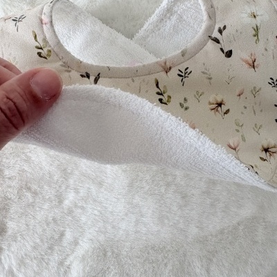 Babete tecido floral bege com interior branco felpudo e mão segurando uma parte