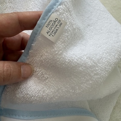 Toalha branca de algodão com borda azul clara e etiqueta visível