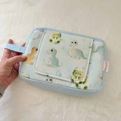 Bolsa de tecido azul claro com desenhos de dinossauros e sapos, segurada por uma mão.