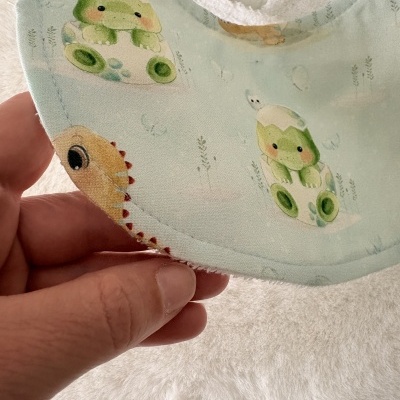 Babete azul claro com desenhos de sapos bebés em casca de ovo