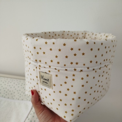 Cesto de tecido branco com estrelas douradas e etiqueta Mamã pintinha segurado por mão feminina