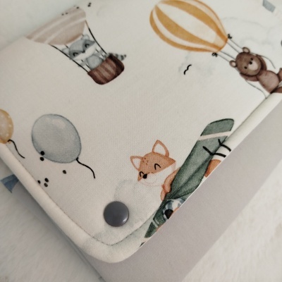 Toalha com desenhos de animais e balões, botão escuro para fechar.