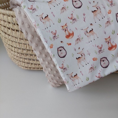 Manta dupla face para bebé com padrão de animais da floresta e textura aveludada, sobre cesta de fibras naturais