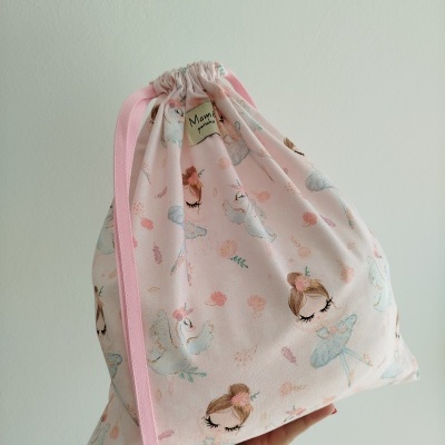 Saco de tecido rosa com desenhos de bailarinas, flores e pássaros segurado por uma mão