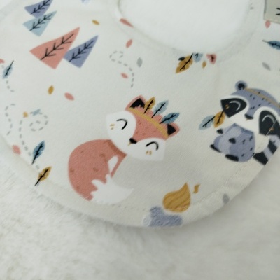 Babete de tecido com desenho de raposa e guaxinim em tons pastel.