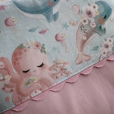 Toalha ou manta infantil com padrão de animais marinhos fofos e borda ondulada rosa.