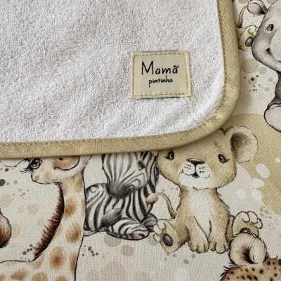 Toalha branca felpuda com borda bege e etiqueta com texto Mamã pintinha sobre tecido estampado com animais bebés.