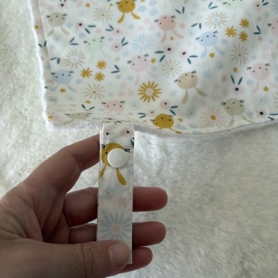 tecido branco com padrão de coelhinhos coloridos e flores, alça com botão branca