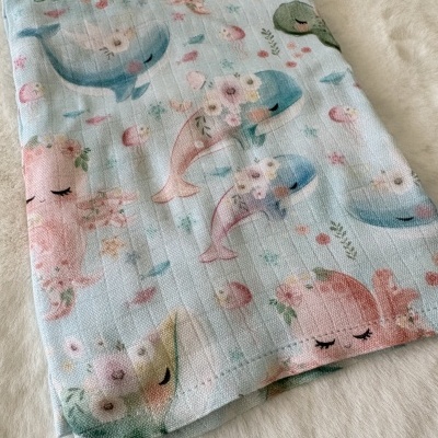 tecido estampado com golfinhos e polvos em tons pastel sobre superfície de pelúcia creme
