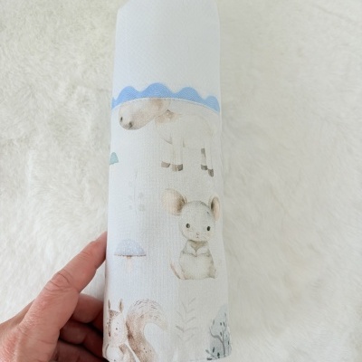 Frasco coberto por tecido estampado com animais e elementos naturais em tons suaves, segurado por uma mão