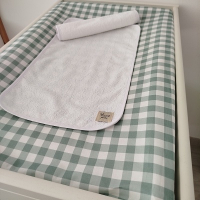 Colchão de bebé verde e branco com toalha branca felpuda e etiqueta