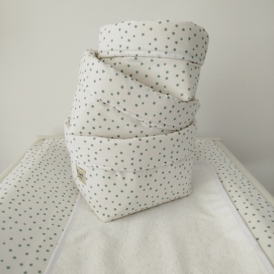 Três cestos de tecido branco com padrão de estrelas verdes empilhados sobre trocador com o mesmo padrão.