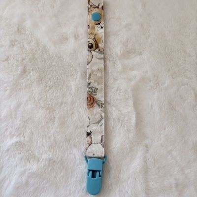 Tira de tecido com padrão canino e floral com botão azul e presilha azul em fundo branco felpudo