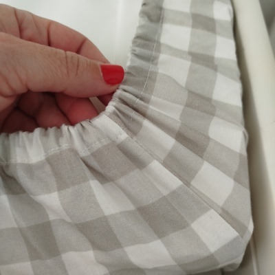 Lençol ajustável xadrez cinza e branco com elástico segurado por mão com unhas vermelhas