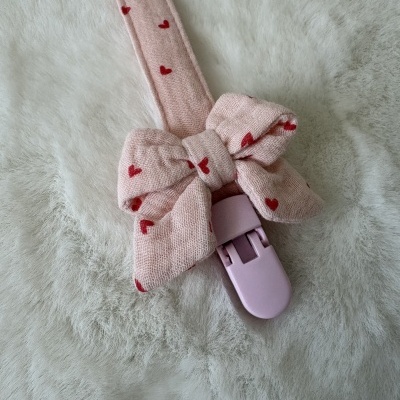 Prendedor de tecido rosa claro com corações vermelhos e laço sobre tecido branco macio