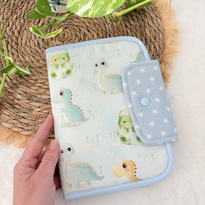 Capa de tecido com padrão de dinossauros e fecho azul com estrelas