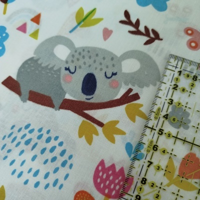 Tecido branco com padrão de coala e elementos naturais coloridos, régua transparente ao lado