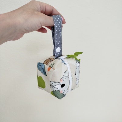 Cubo de tecido com padrão de coala e folhas, alça cinza com pontos brancos, fecho de correr branco