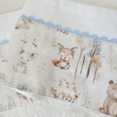 Toalha branca com faixa decorativa ilustrada com animais em tons pastel e borda azul clara ondulada