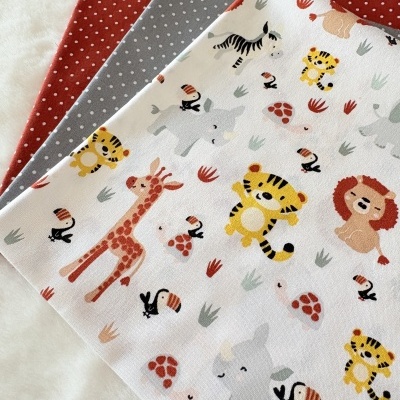 Três tecidos dobrados com padrões diferentes, incluindo animais da selva e bolinhas.