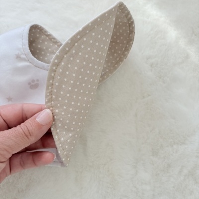Babete para bebé bege com bolinhas brancas e lado exterior branco com patinhas e estrelas cinza claro