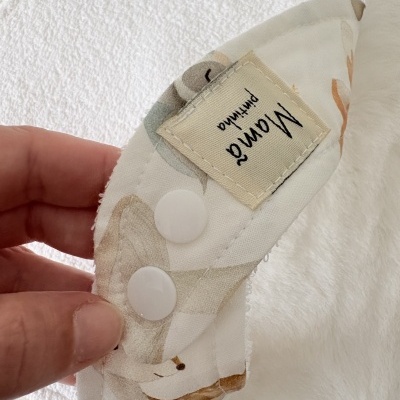 Pano de tecido com padrão e botões brancos, etiqueta com texto Mama pintinho.