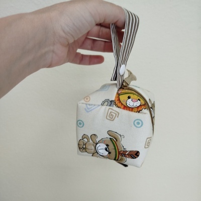 Bolsa de tecido pequena com padrão de animais e alça riscada, segurada por mão.