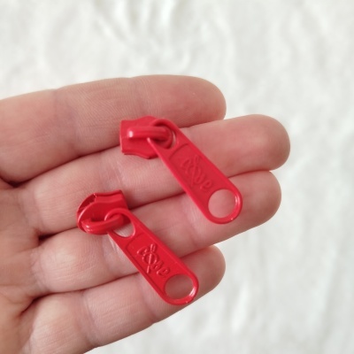 Dois puxadores vermelhos para fecho éclair com a palavra Love gravada numa mão sobre fundo branco desfocado