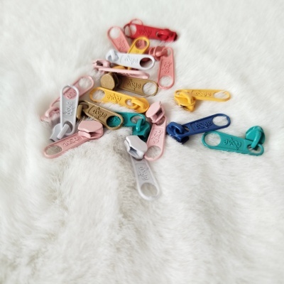 Puxadores de zíper coloridos em plástico sobre tecido branco macio.