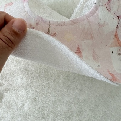 Babete infantil rosa com castelos e unicórnios, com interior de tecido de rizo branco