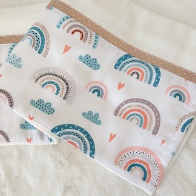 Colchas brancas com decoração de arco-íris coloridos e corações, barra bege com pontos, sobre superfície branca peluda
