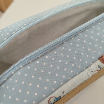Estojo azul claro com bolinhas brancas e fecho de correr azul aberto mostrando interior cinzento claro
