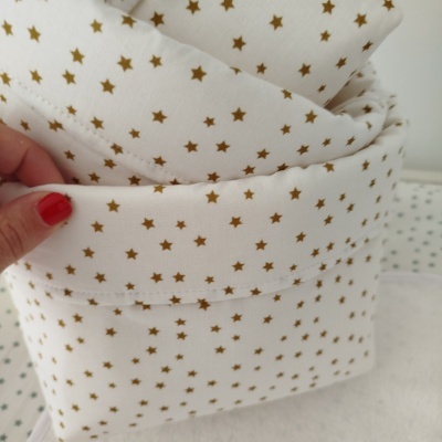 Tecido branco com pequenas estrelas douradas e costura visível, segurado por mão com unhas vermelhas