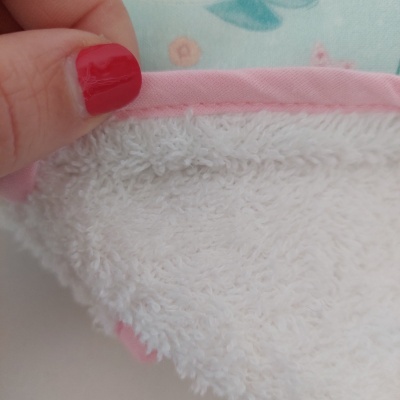 Toalha branca com borda rosa e unha pintada de vermelho segurando a toalha