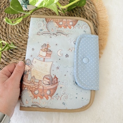 Capa de tecido azul claro com ilustração náutica infantil e fecho azul de bolinhas brancas.