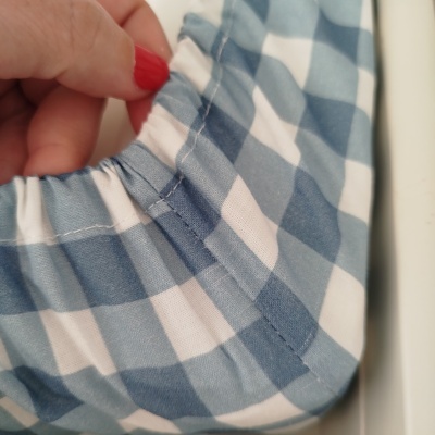 Pano azul e branco com padrão xadrez e elástico sendo segurado por mão com unhas vermelhas